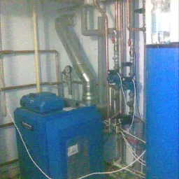 Niebieski piec CO marki Buderus w kotłowni z widocznymi rurami miedzianymi i białymi kablami.